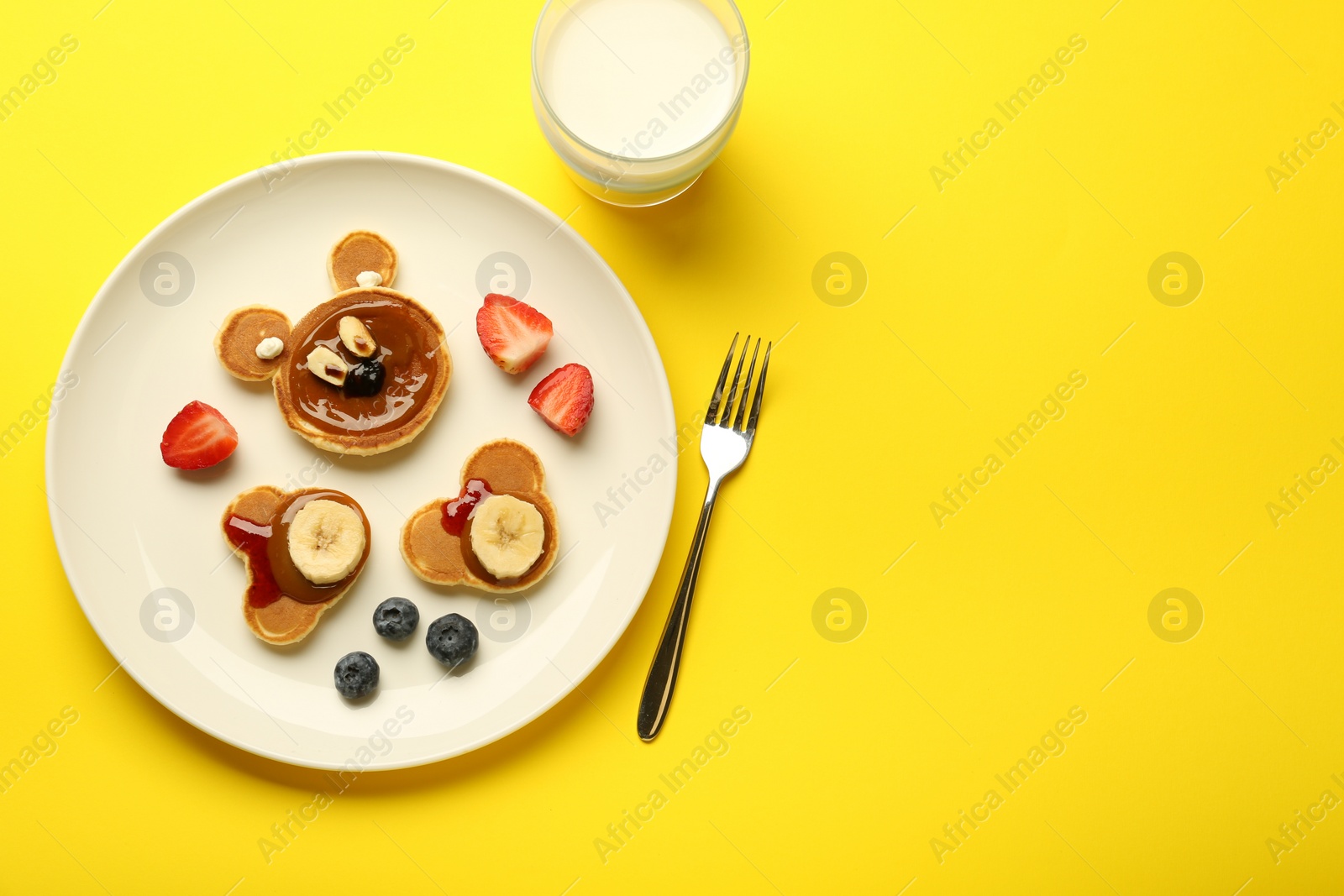 Photo of Creative serving for kids. Plate with cute bears made of pancakes, berries, banana and chocolate paste on yellow background, flat lay. Space for text