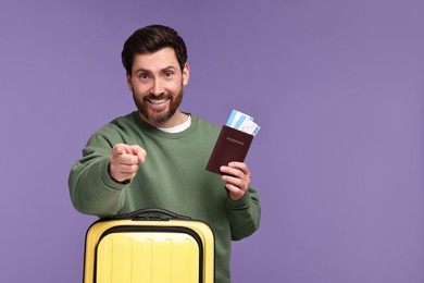 Photo of Smiling man with passport, tickets and suitcase on purple background. Space for text