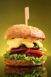 Delicious vegetarian burger on mirror surface against olive background