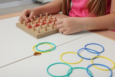 Motor skills development. Girl playing with geoboard and rubber bands at white table, closeup