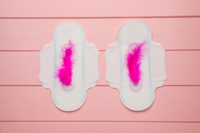 Menstrual pads with feathers on pink wooden background, flat lay