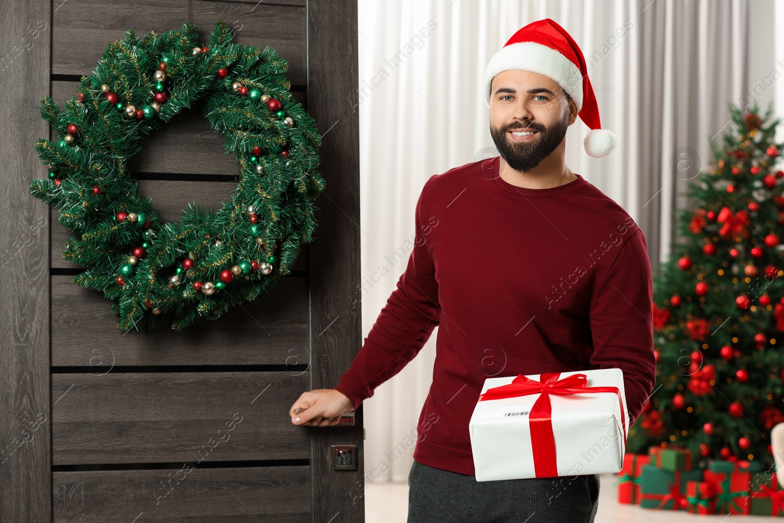 Photo of Young man in Santa hat with Christmas gift box received by mail indoors