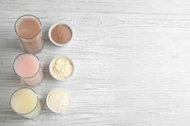 Protein shakes and powder on white wooden table, flat lay. Space for text