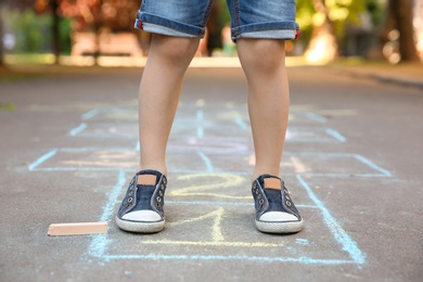 Photo of Little child playing hopscotch drawn with colorful chalk on asphalt