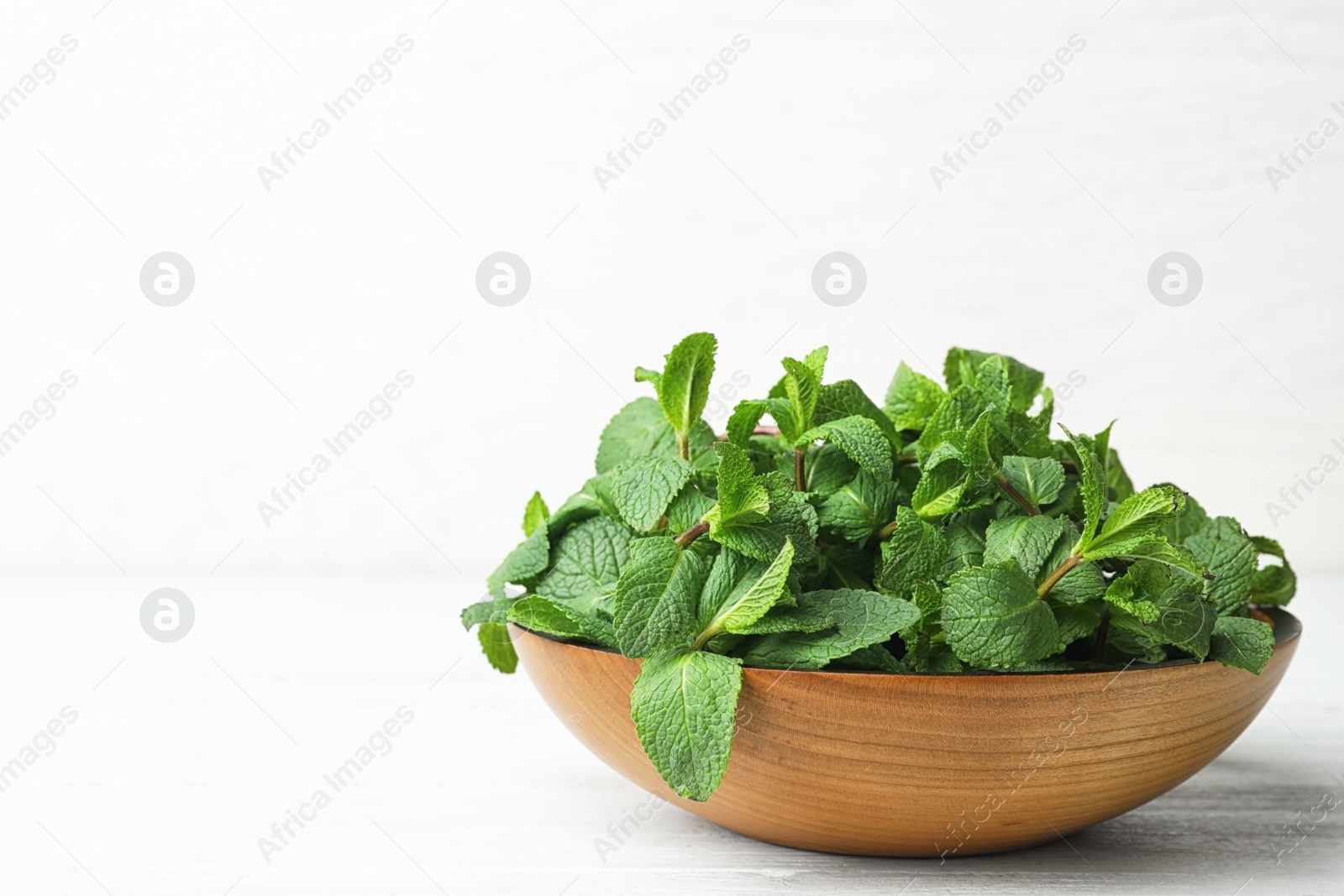 Photo of Wooden bowl with fresh green mint on table. Space for text