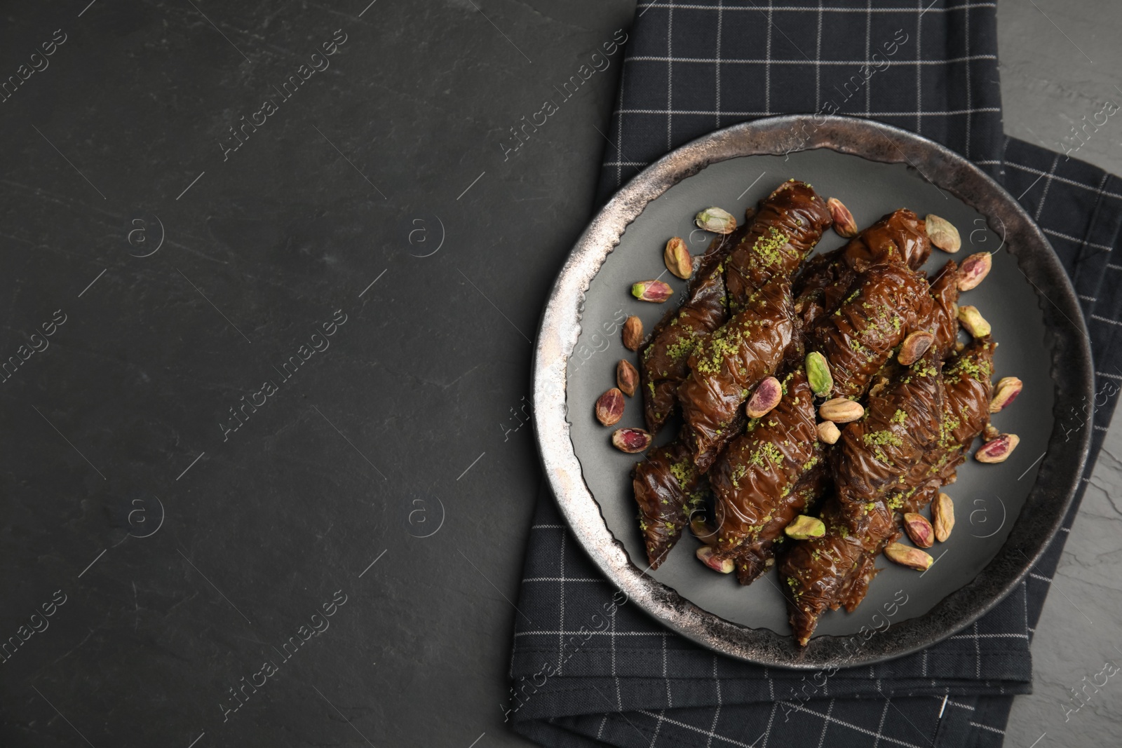 Photo of Delicious baklava with pistachio nuts and napkin on black table, top view. Space for text