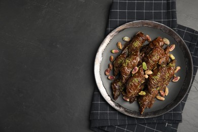 Delicious baklava with pistachio nuts and napkin on black table, top view. Space for text