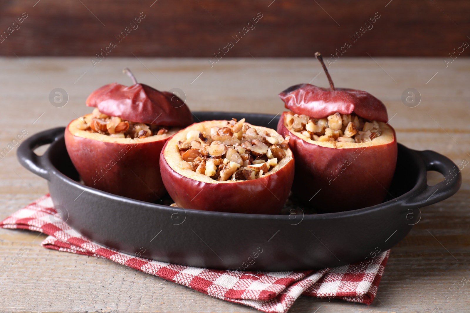 Photo of Tasty baked apples with nuts in baking dish on wooden table, closeup