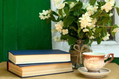 Photo of Books, cup of aromatic drink and beautiful jasmine flowers on wooden table near window outdoors