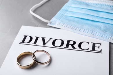 Composition with protective mask and wedding rings on grey table, closeup. Divorce during coronavirus quarantine