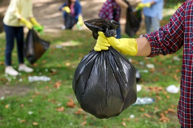 Man holding plastic bag with garbage in park, closeup