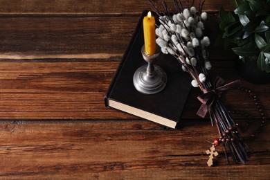 Rosary beads, Bible, burning candle and willow branches on wooden table, above view. Space for text