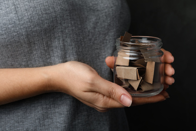 Woman holding glass jar with paper pieces, closeup on hands