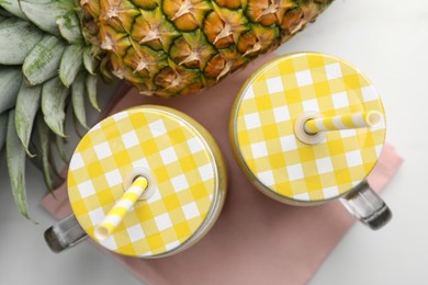 Photo of Tasty pineapple smoothie in mason jars and fruit on white table, flat lay