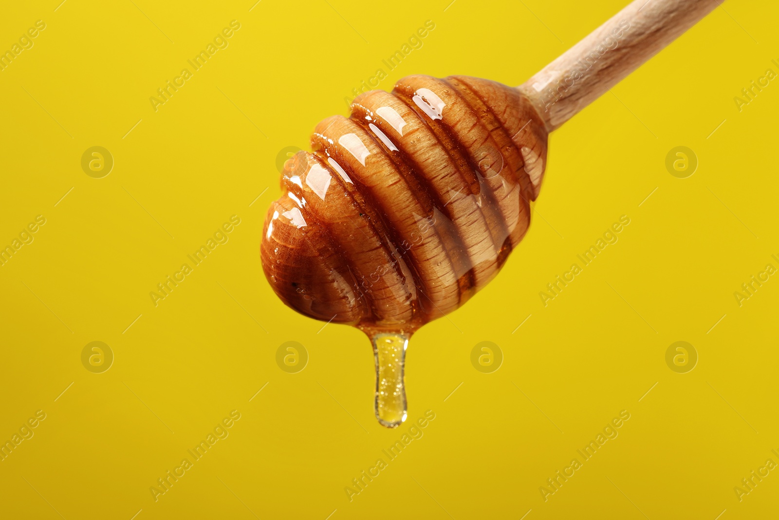 Photo of Delicious honey flowing down from dipper against yellow background, closeup