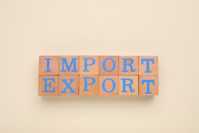 Photo of Words Import and Export made of wooden cubes with letters on beige background, top view