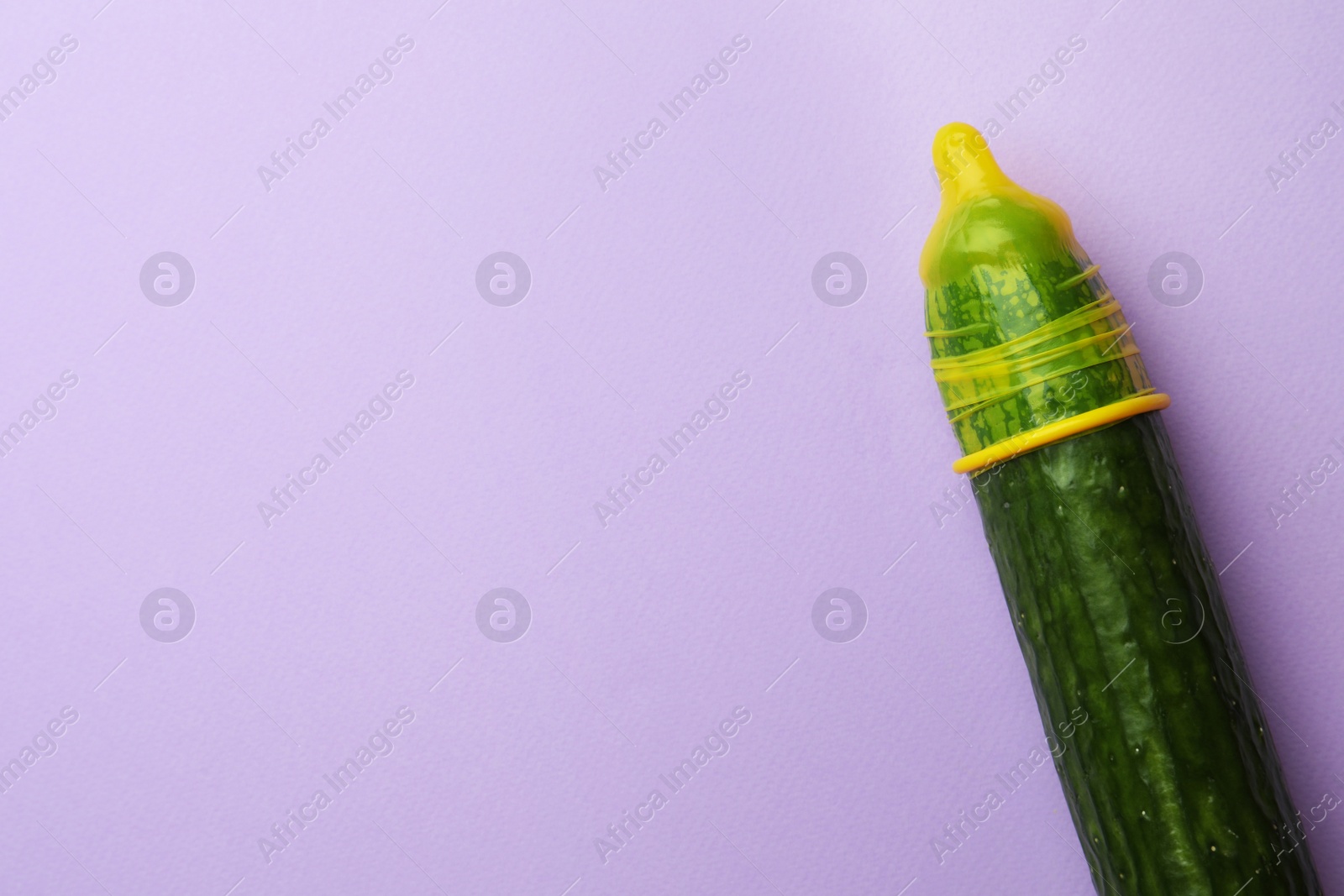 Photo of Cucumber with condom on lilac background, top view and space for text. Safe sex concept