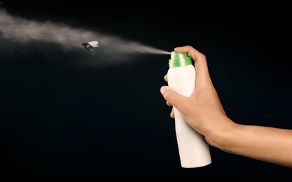 Woman spraying insect aerosol on fly against black background, closeup