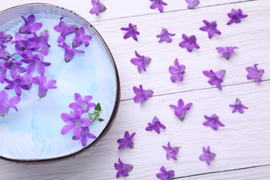 Photo of Bowl with water and flowers on white wooden table, flat lay. Spa composition