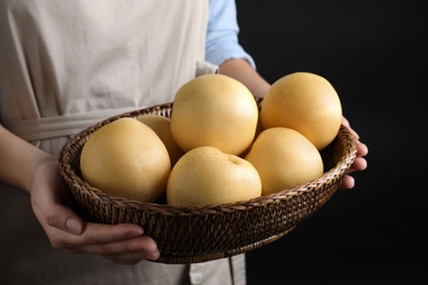 Woman holding wicker bowl ripe apple pears on black background, closeup