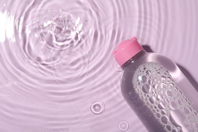 Photo of Wet bottle of micellar water on violet background, top view. Space for text