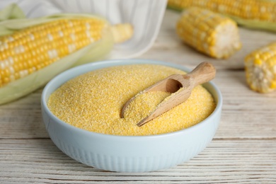 Photo of Cornmeal in bowl and fresh cobs on white wooden table