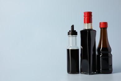Bottles with soy sauce on light grey background, space for text