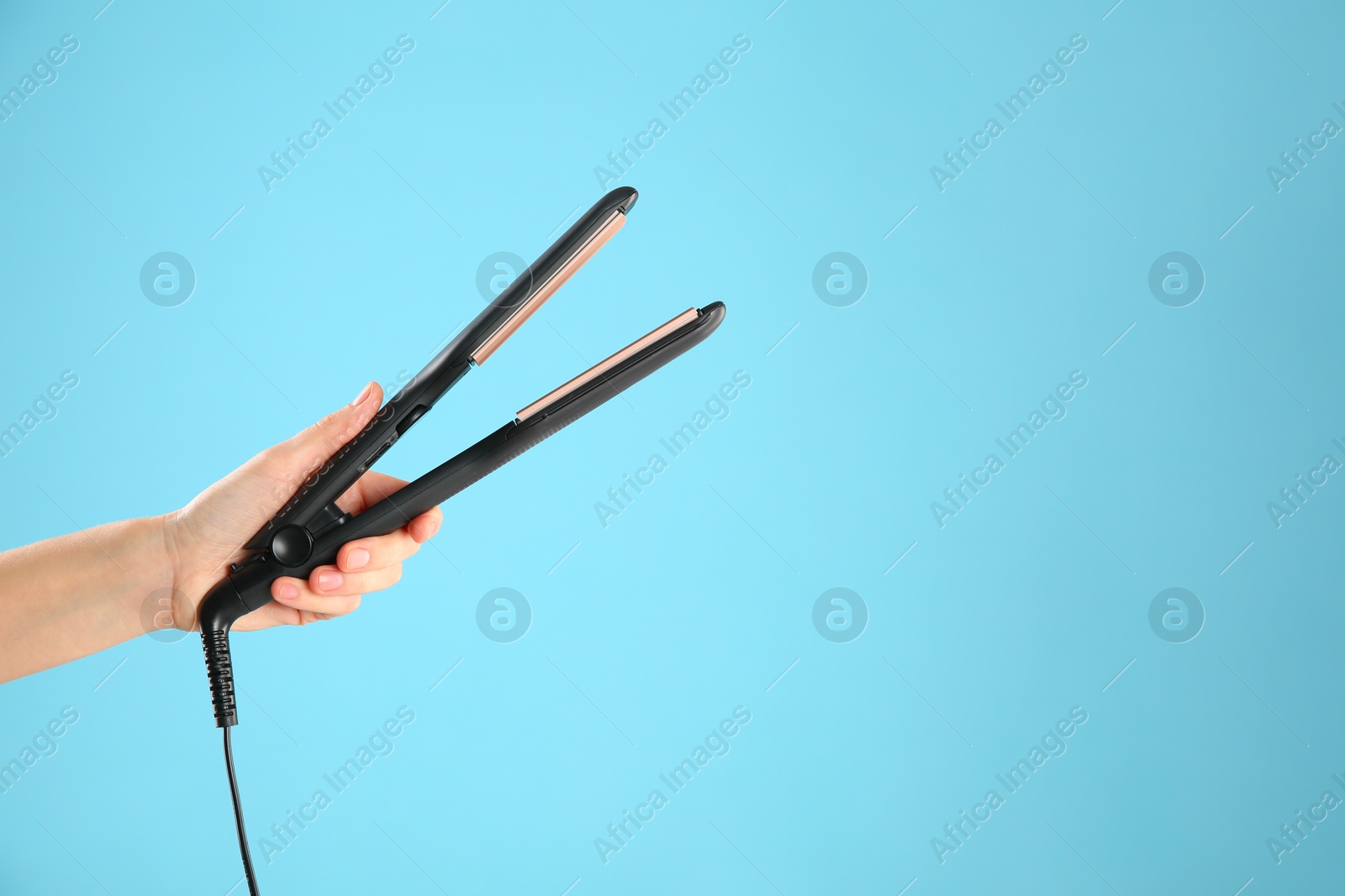 Photo of Woman holding corrugated hair iron on light blue background, closeup