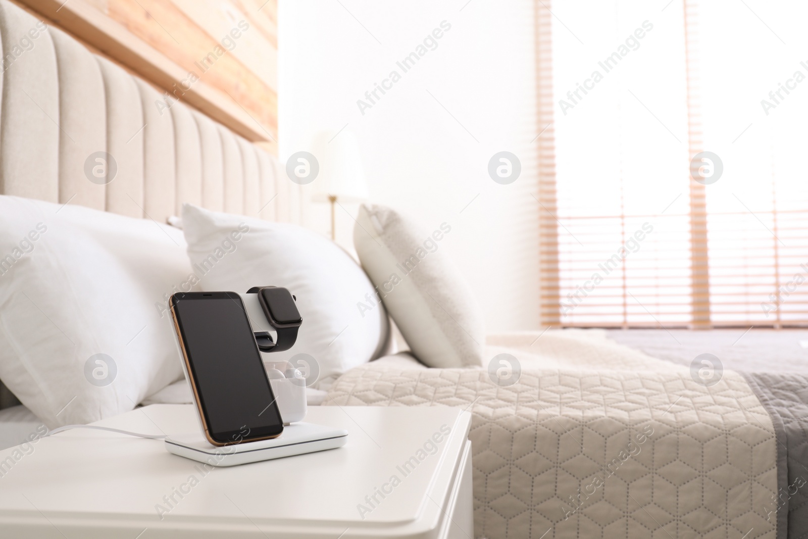 Photo of Different gadgets charging on wireless pad in bedroom. Space for text