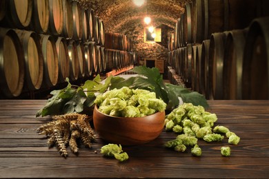Image of Fresh hops and wheat spikes on wooden table in beer cellar