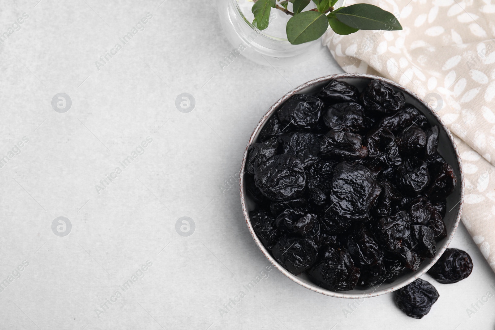 Photo of Bowl with sweet dried prunes on light table, top view. Space for text