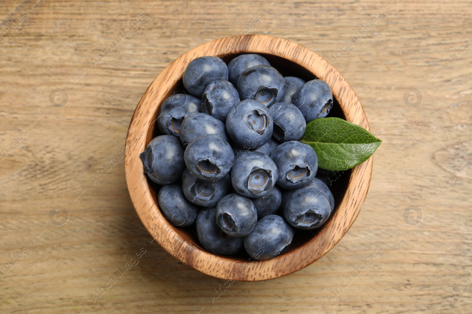 Photo of Bowl of fresh tasty blueberries on wooden table, top view