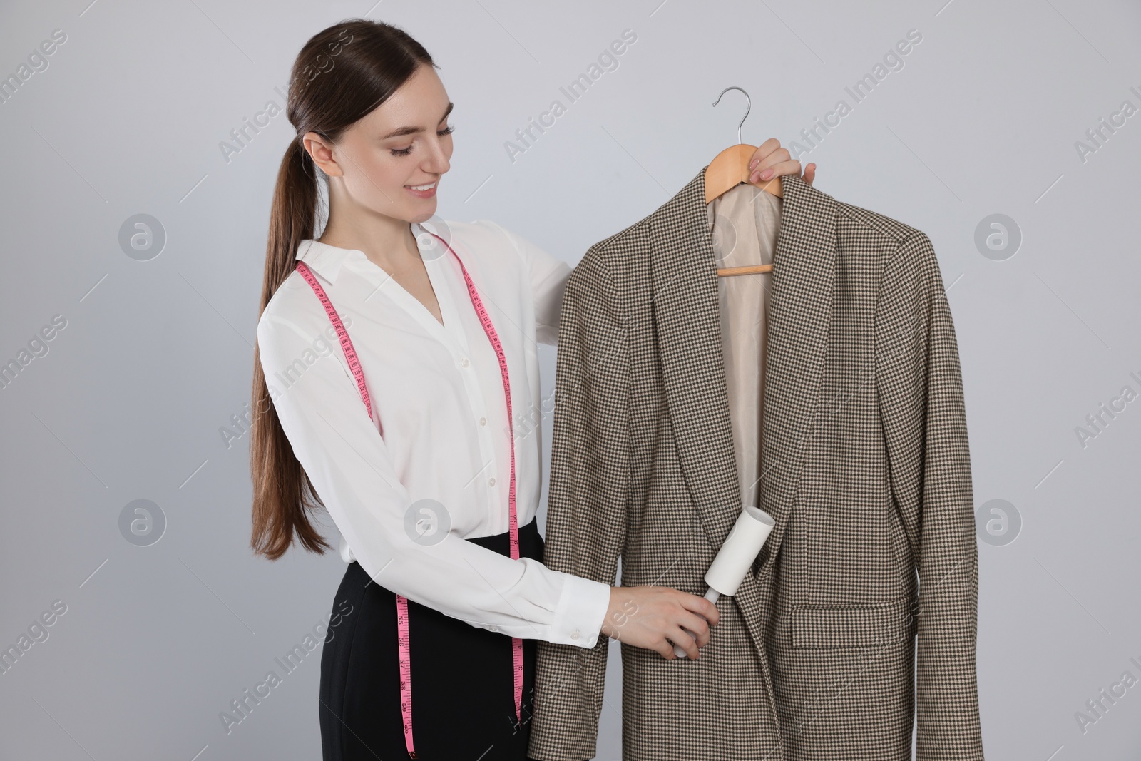 Photo of Young woman using adhesive lint roller on light grey background. Dry-cleaning service