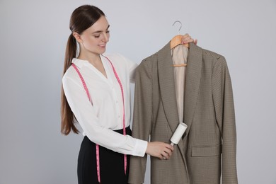 Photo of Young woman using adhesive lint roller on light grey background. Dry-cleaning service