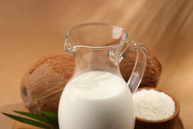 Photo of Glass jug of delicious vegan milk near coconuts on brown background, closeup