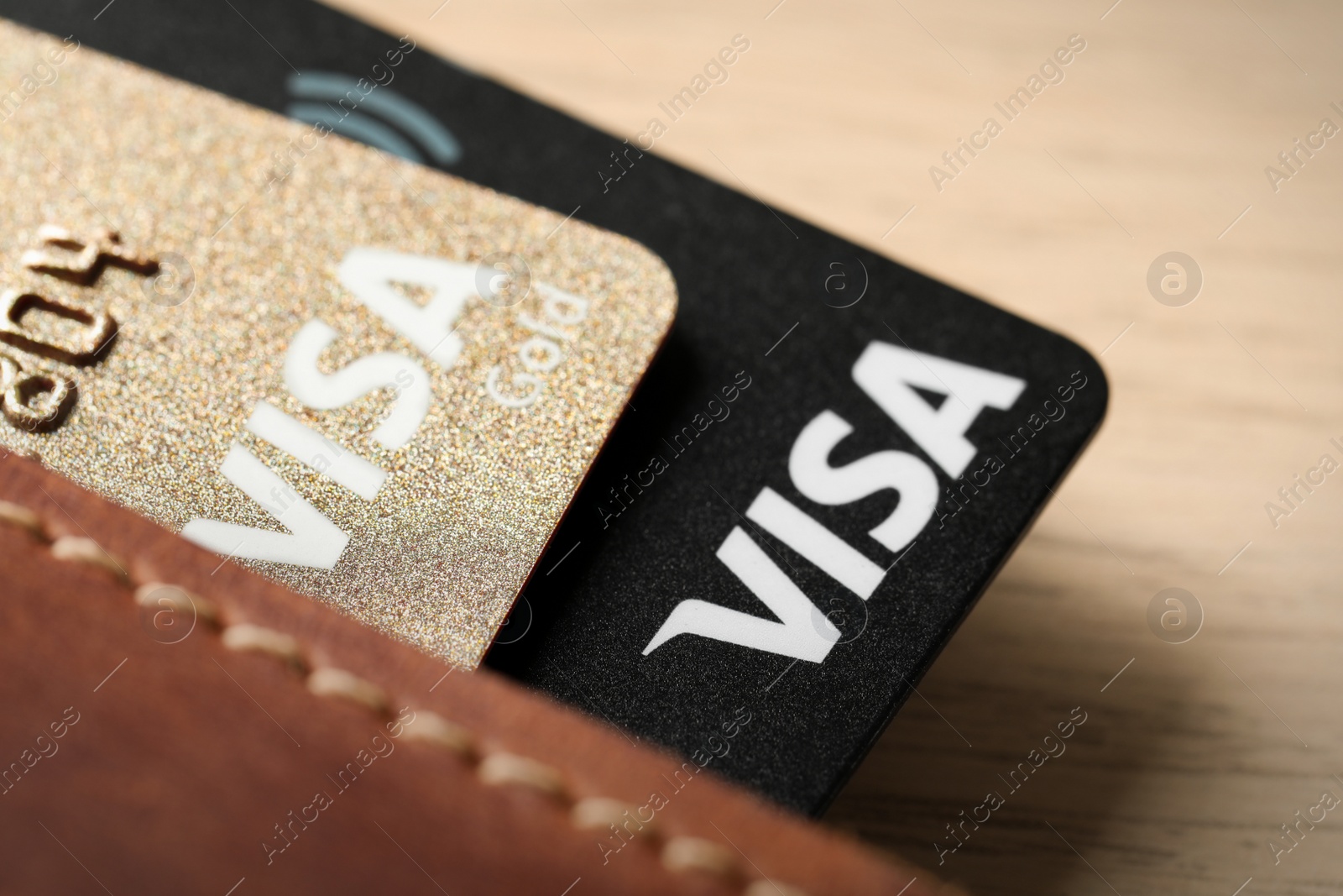 Photo of MYKOLAIV, UKRAINE - FEBRUARY 23, 2022: Bank cards of Visa payment system in leather wallet on wooden table, closeup