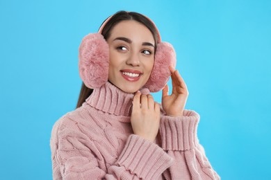 Photo of Beautiful young woman wearing earmuffs on light blue background