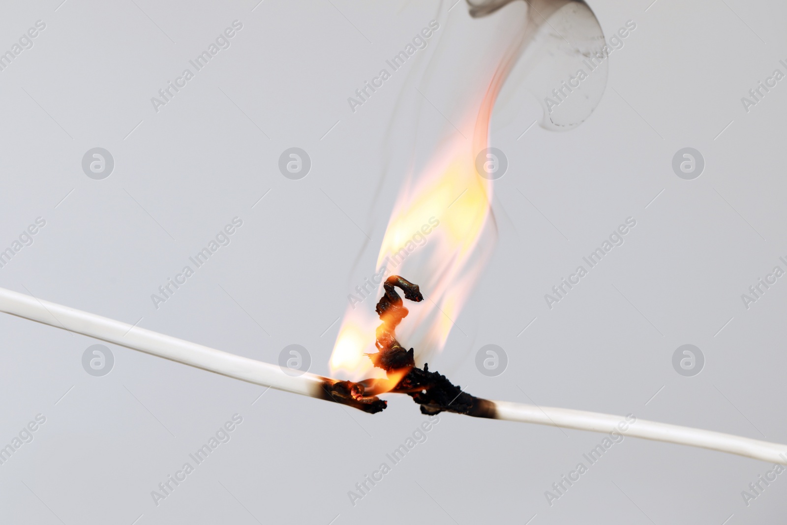 Photo of Inflamed white wire on grey background, closeup. Electrical short circuit