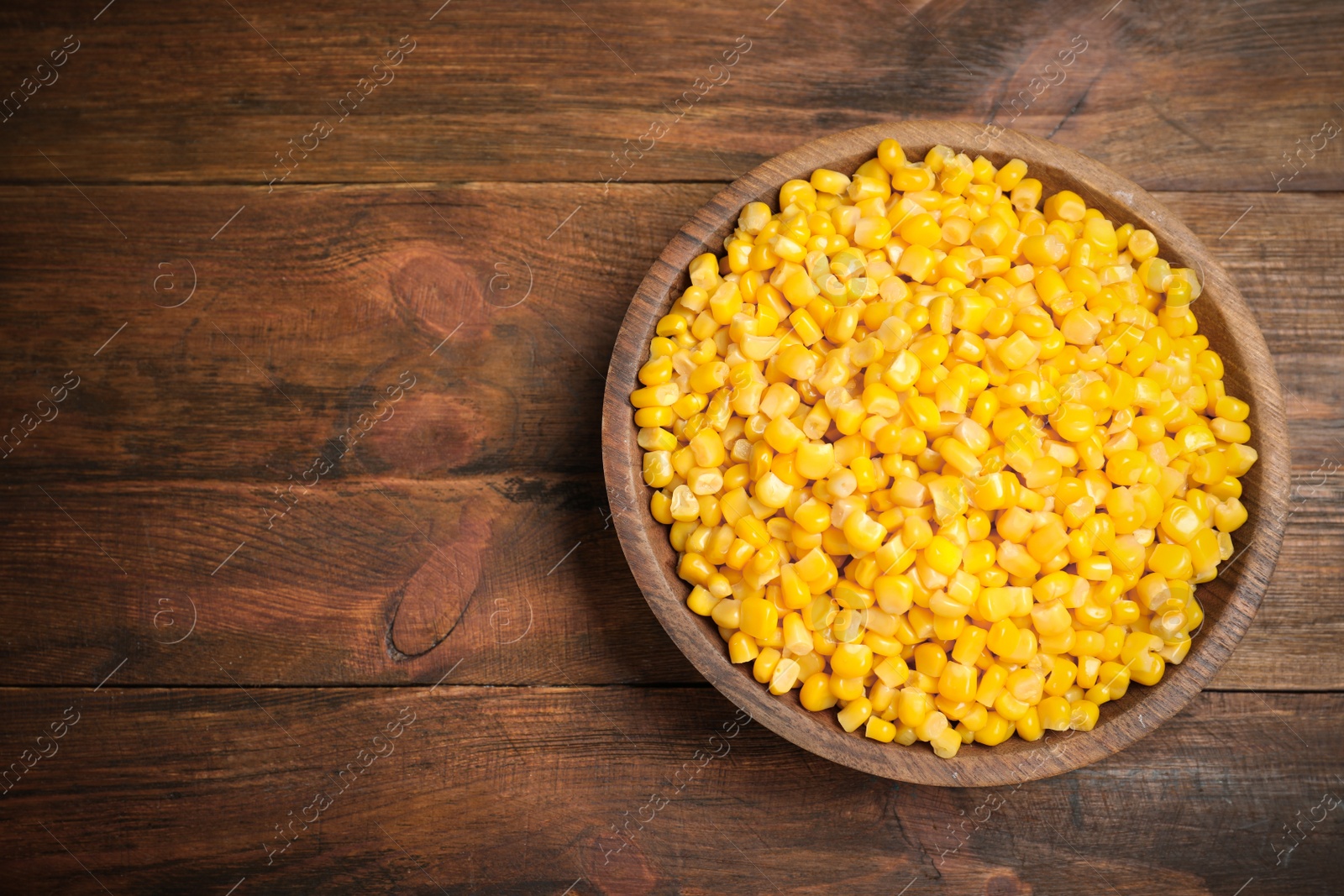 Photo of Delicious canned corn in bowl on wooden table, top view. Space for text