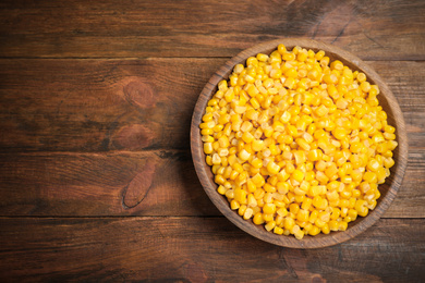 Photo of Delicious canned corn in bowl on wooden table, top view. Space for text