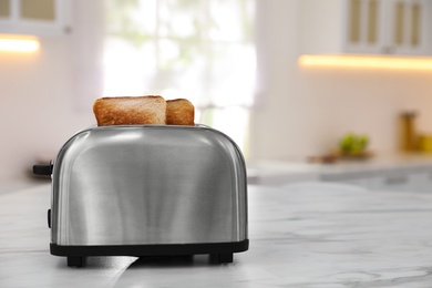 Photo of Modern toaster with slices of bread on table in kitchen. Space for text
