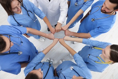 Doctor and interns holding fists together indoors, top view