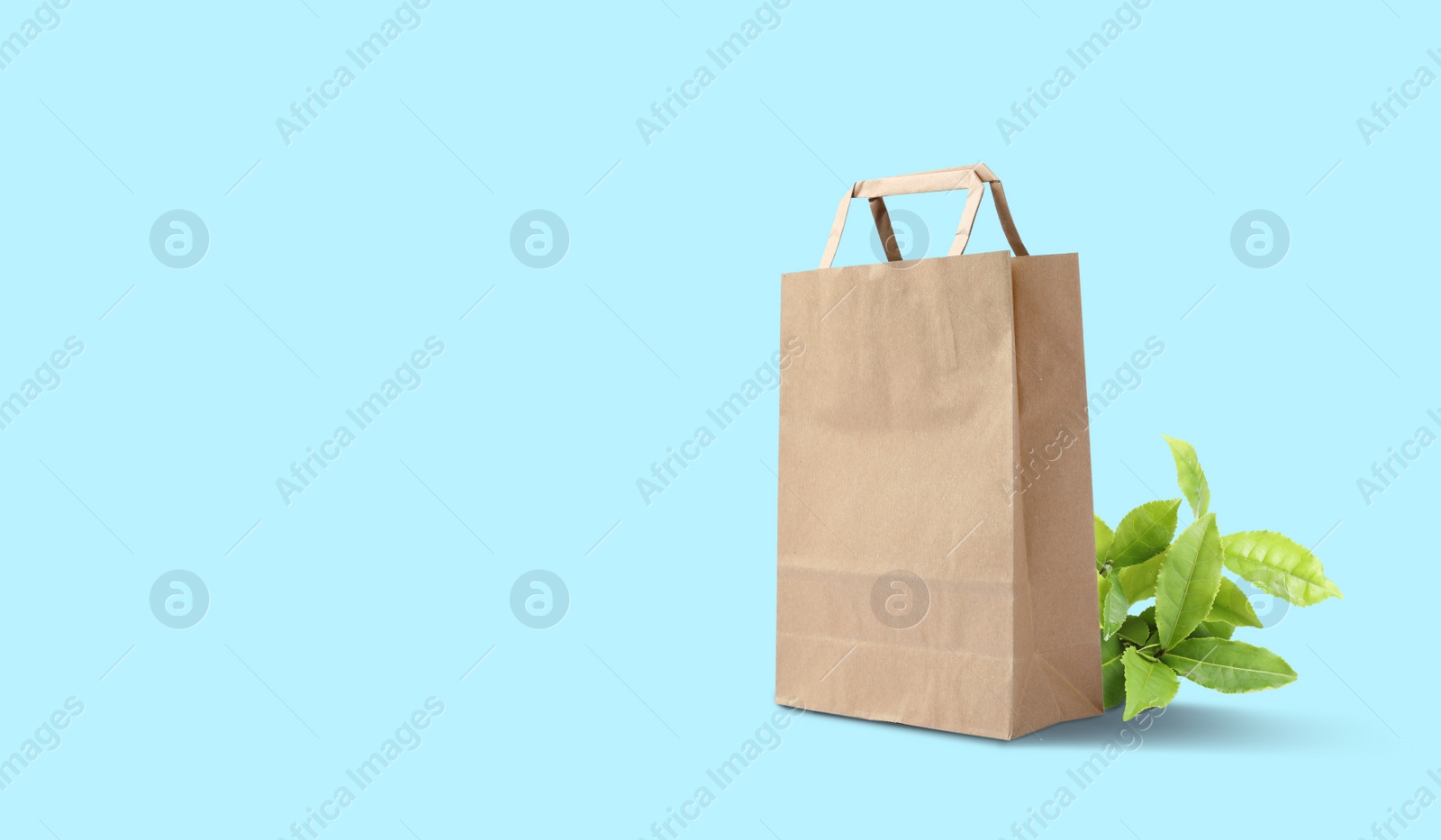Image of Paper shopping bag and green leaves on cyan background, space for text. Eco friendly lifestyle