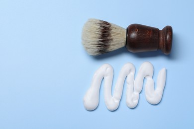 Sample of shaving foam and brush on light blue background, flat lay. Space for text