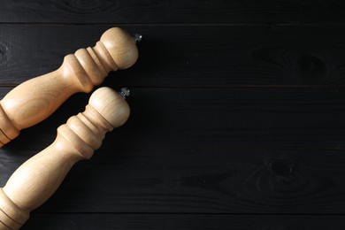 Salt and pepper shakers on black wooden table, flat lay. Space for text