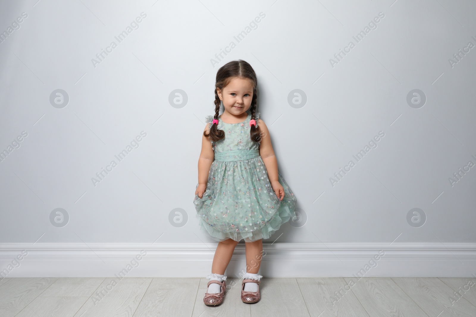 Photo of Cute little girl near light grey wall