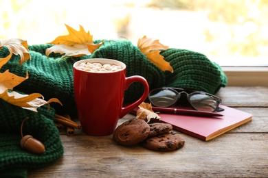 Photo of Composition with cup of hot drink, sweater and autumn leaves on windowsill. Cozy atmosphere