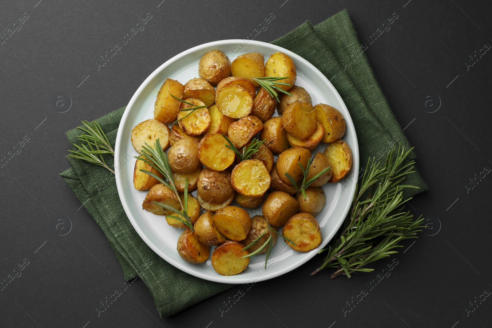 Photo of Delicious baked potatoes with rosemary on black table, top view