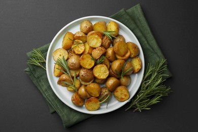 Delicious baked potatoes with rosemary on black table, top view