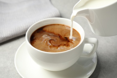 Photo of Pouring milk into cup of hot coffee on grey table, closeup